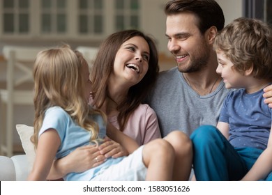 Happy married couple holding on lap little son and daughter enjoy time together on weekend free time at home, relative people laughing communicating having warm relations showing love and care concept