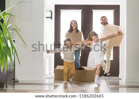 Happy married couple and little children arrive at new modern house. Husband and wife with cardboard boxes look at running inside excited daughter and son. Buy realestate, mortgage and moving concept