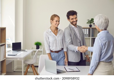 Happy Married Couple Shaking Hands With A Female Lawyer, Realtor Or Financial Advisor. Man And Woman At A Reception At An Insurance Broker Or Bank Employee. Concept Of Business Ethics And Trust.