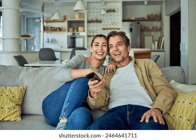 A happy married couple sitting on the couch at home and searching for a movie to watch on the TV, using a remote. - Powered by Shutterstock