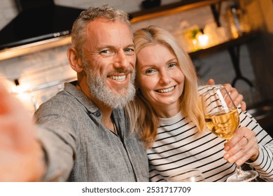 Happy married couple taking selfie while on a romantic date in the kitchen. Husband and wife, spouses, girlfriend and boyfriend streaming online on anniversary Valentine`s Day - Powered by Shutterstock