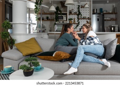 Happy Married Homosexual Female Gay Couple Laughing And Embracing On The Sofa With Smile On Their Faces. Lesbian Couple At Home Enjoying Life Together In Their New Apartment.