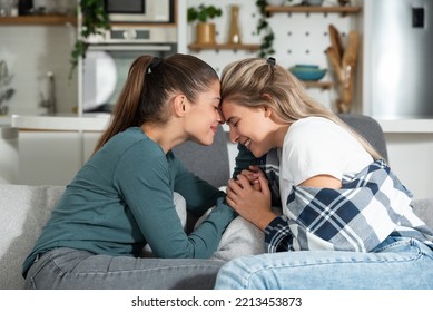 Happy Married Homosexual Female Gay Couple Laughing And Embracing On The Sofa With Smile On Their Faces. Lesbian Couple At Home Enjoying Life Together In Their New Apartment.