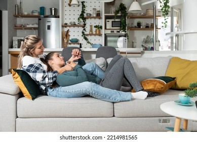 Happy Married Homosexual Female Gay Couple Laughing And Embracing On The Sofa With Smile On Their Faces. Lesbian Couple At Home Enjoying Life Together In Their New Apartment.