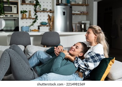 Happy Married Homosexual Female Gay Couple Laughing And Embracing On The Sofa With Smile On Their Faces. Lesbian Couple At Home Enjoying Life Together In Their New Apartment.