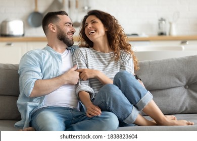Happy married young couple hugging, sitting on cozy couch together, overjoyed laughing woman and man having fun, enjoying leisure time, relaxing on sofa in living room at home, good relationship - Shutterstock ID 1838823604