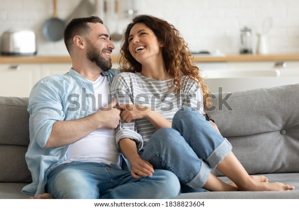 Happy Married Young Couple Hugging Sitting On Cozy Couch Together Overjoyed Laughing Woman And