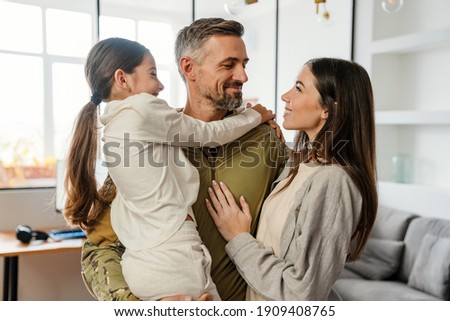 Happy masculine military man smiling and hugging his family indoors