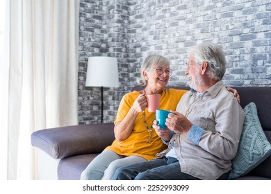 Happy mature 50s husband and wife sit rest on comfortable sofa in living room enjoy tea talking, smiling elderly 60s couple relax on couch at home drink coffee chat speak laugh on leisure weekend - Powered by Shutterstock