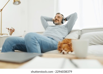 Happy Mature Adult man sitting on sofa relaxing  and listening to music with headphones in living room at home. Senior male sleeping on couch with his chihuahua dog. Well-being, lifestyle, recreation - Powered by Shutterstock