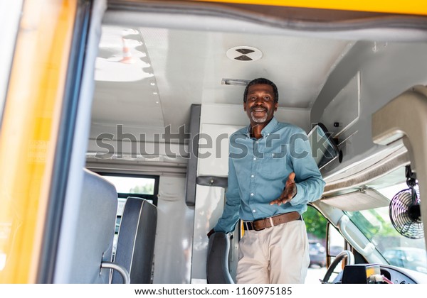 happy mature african american bus driver
standing inside bus and looking at
camera