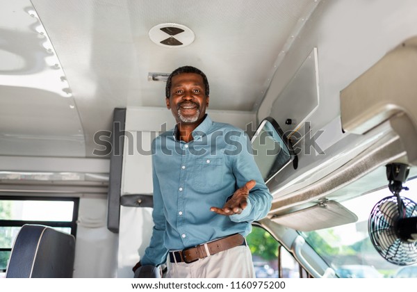 happy mature african american bus driver\
standing inside bus and looking at\
camera