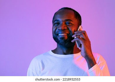 Happy Mature African American Man In White Having Phone Conversation With Someone And Smiling, Holding Cell Phone Next To Ear, Looking At Copy Space, Closeup Studio Shot, Neon Background