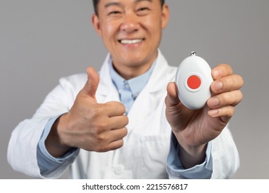 Happy Mature Asian Male Doctor In White Coat Shows Alarm Button And Thumb Up Isolated On Gray Background, Studio, Close Up, Cropped. Recommendation, Advice, Medical Service And Emergency Health Care