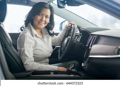 Happy Mature Asian Woman Smiling To The Camera Joyfully Sitting In A Car At The Dealership Showroom Copyspace Owning Buying Choosing Vehicle Transport Automobile Comfort Luxury Lifestyle Driving