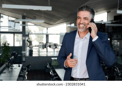 Happy mature business man ceo standing in office talking on cell phone. Middle aged businessman professional executive manager holding smartphone making corporate call communicating with client.
