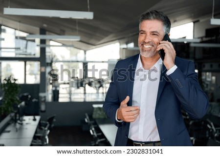Happy mature business man ceo standing in office talking on cell phone. Middle aged businessman professional executive manager holding smartphone making corporate call communicating with client.
