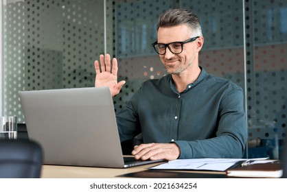 Happy Mature Business Man Executive Waving Hand Using Laptop Computer Having Video Conference Call Virtual Meeting, Professional Training Negotiation Remote Working Online In Office. Videoconference