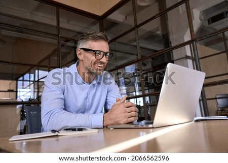 Happy mature business man executive manager looking at laptop computer watching online webinar or having remote virtual meeting, video conference call negotiation corporate training working in office.