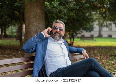 A Happy Mature Business Man Talking On Mobile Phone While Siting At The Park Bench.