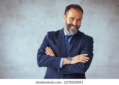Happy mature business professional standing with his arms crossed in modern office. Smiling businessman at his workplace. Successful Mature man with folded arms standing over grey background.  - Shutterstock ID 2278103091