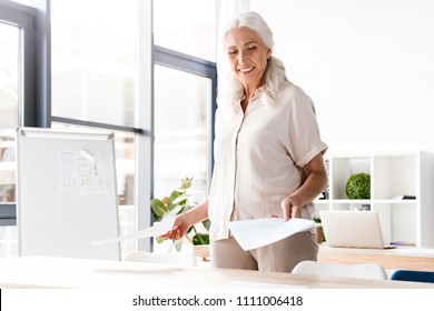 Happy Mature Business Woman Analyzing Documents While Standing At Her Desk In Office