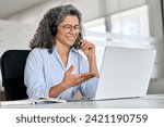 Happy mature business woman call centre representative customer support agent talking to client, smiling middle aged senior female operator wearing headset working using laptop computer in office.