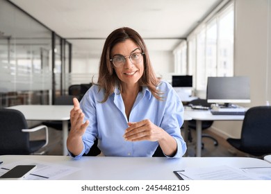 Happy mature business woman middle aged female hr manager executive looking at web camera sitting at work desk talking having hybrid office meeting or online job interview. Web cam screenshot. - Powered by Shutterstock