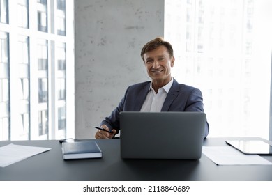 Happy mature businessman, company executive, CEO head shot portrait. Male business leader, professional, project owner sitting at work desk, laptop computer, looking at camera, smiling,