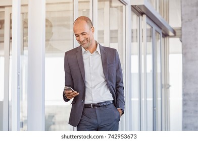 Happy Mature Businessman In Formal Using Smartphone In Modern Office. Successful Senior Business Man Smiling On Reading Message On Cellphone. Man Using Mobile Phone In Office.