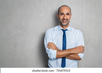 Happy Mature Businessman In Shirt And Tie Looking At Camera. Portrait Of Smiling And Satisfied Hispanic Business Man With Arms Crossed Isolated Over Grey Background With Copy Space. Successful Senior 