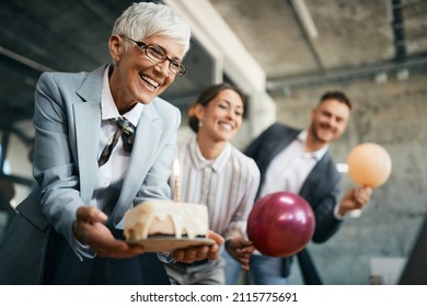 Happy Mature Businesswoman Holding Birthday Cake While Throwing Surprise Party With Her Associates In The Office.  