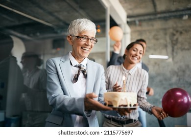 Happy Mature Businesswoman Holding Birthday Cake While Making Surprise Party With Her Colleagues In The Office.