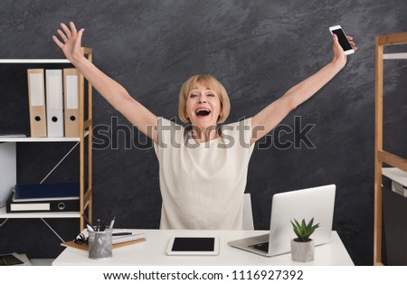 Happy mature businesswoman in office. Accountant sitting with raised arms, enjoying new achievement