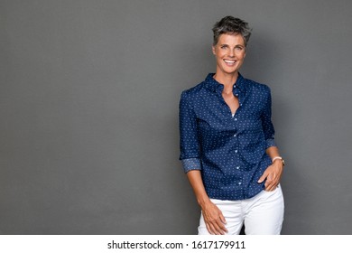 Happy mature businesswoman standing on grey background. Successful senior business woman with hand in pocket looking at camera. Portrait of confident and reliable lady standing against gray wall.