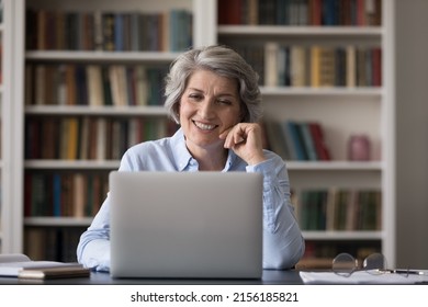 Happy mature businesswoman talking on video call at laptop in office, smiling, laughing, enjoying using online app. Senior student studying in library, watching learning webinar - Powered by Shutterstock