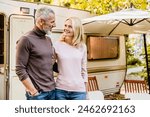 Happy mature caucasian couple looking at each other with passion and love near their caravan home. Traveling together, escaping the urban life by trailer motor home camper van