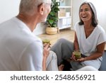 Happy mature caucasian woman drinking healthy green vegetable juice after exercising at home with husband. Healthy and active lifestyle concept.