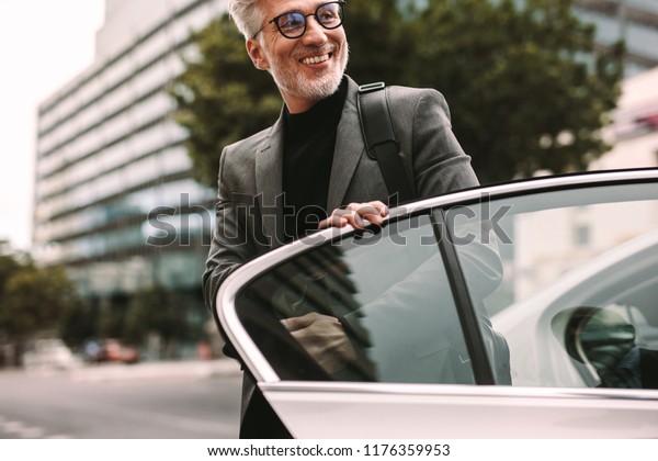 Happy mature commuter getting out of a taxi.\
Businessman getting off a\
cab.