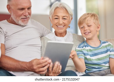 A Happy Mature Couple Bonding With Their Grandchild While Babysitting And Using A Digital Tablet On A Couch At Home. Grandparents Relaxing With Their Cute Little Grandson And Browsing The Internet