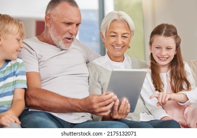 A Happy Mature Couple Bonding With Their Grandchildren While Babysitting And Using A Digital Tablet At Home. Grandparents Relaxing With Their Cute Little Grandson And Granddaughter Browsing Internet