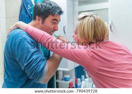Happy mature couple brushing their teeth in the morning, teasing each other, having fun