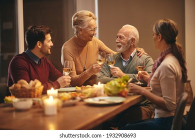 Happy mature couple celebrating and toasting with wine while having dinner with their adult children at dining table.  - Powered by Shutterstock