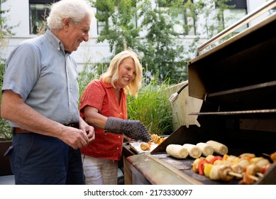 Happy Mature Couple Cooking Kebabs Outside On Their Grill.