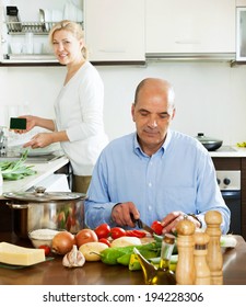 happy mature couple cooking together in kitchen