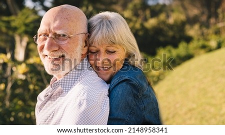 Happy mature couple embracing each other while standing in a park. Romantic elderly couple smiling and enjoying the sun together. Affectionate senior couple spending quality time after retirement.
