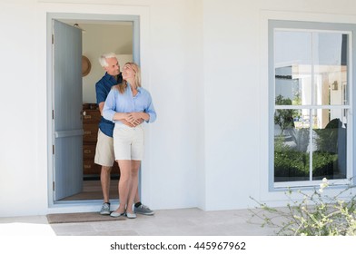 Happy Mature Couple Embracing In Front Of The Door. Smiling Happy Senior Man And Woman Looking At Each Other On The Doorstep Of New House. Smiling Husband Embracing Wife.
