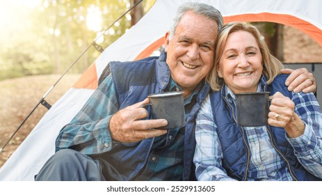 Happy mature couple enjoying camping. Smiling seniors with mugs. Happy elderly pair outdoors. Senior couple camping, smiling, and enjoying nature together. Happy man and woman camping, drinking coffee - Powered by Shutterstock