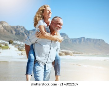 Happy mature couple enjoying vacation by the beach. Active senior husband giving his wife a piggyback ride while enjoying a sunny day outdoors. Energetic man and woman having fun while on holiday - Shutterstock ID 2176022109