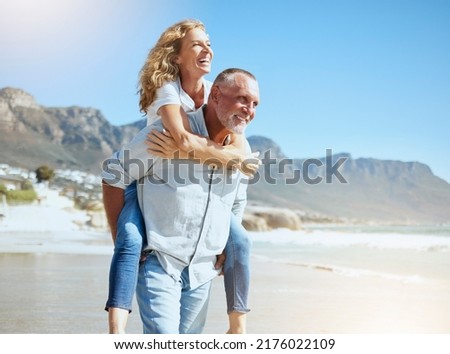 Happy mature couple enjoying vacation by the beach. Active senior husband giving his wife a piggyback ride while enjoying a sunny day outdoors. Energetic man and woman having fun while on holiday